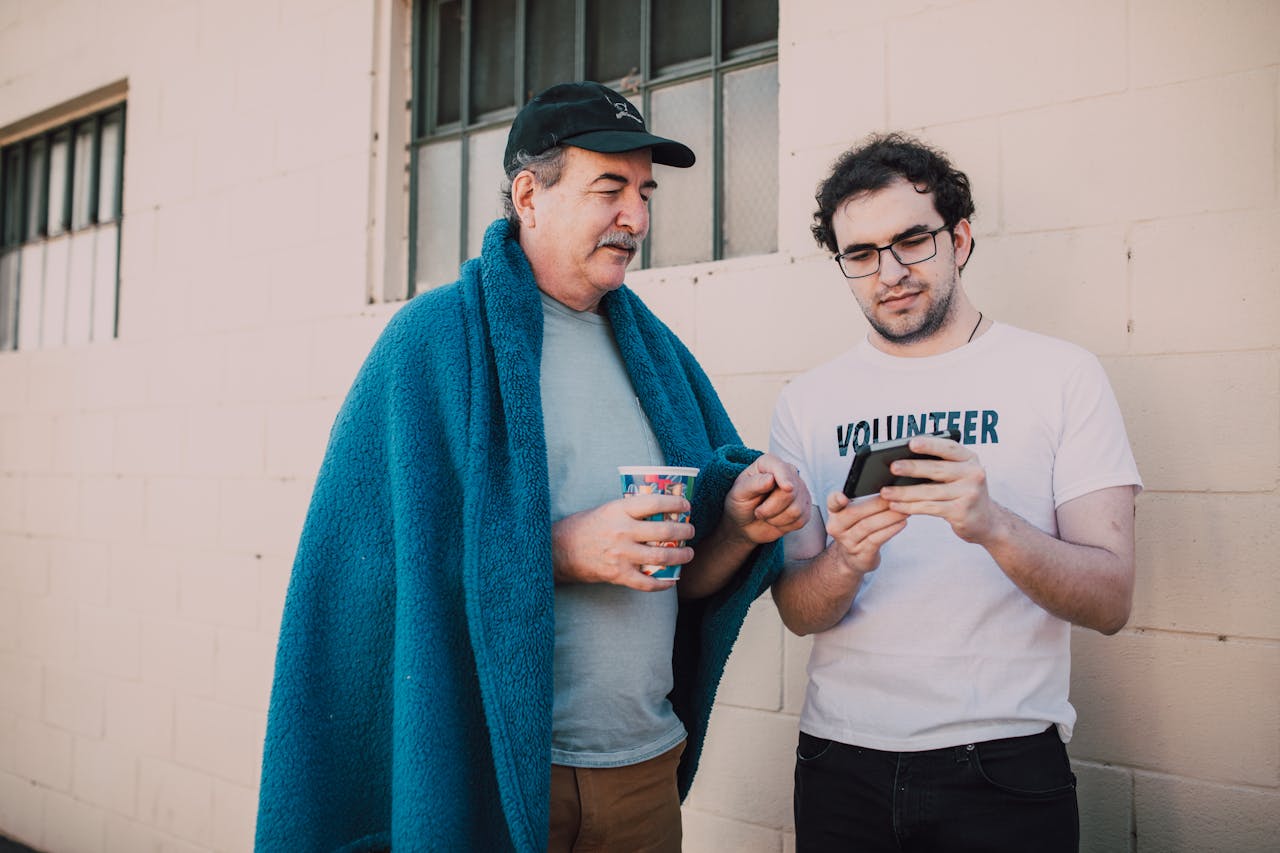 A volunteer helping a homeless man with smartphone services outdoors.